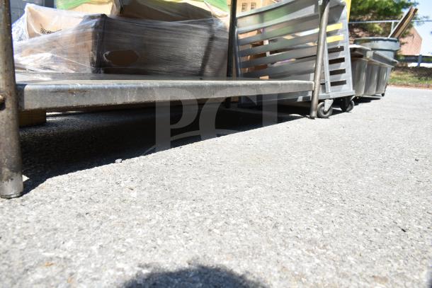 Commercial table with under shelf, metal frame, caster wheels, slightly worn condition. Ideal for storage and mobility.