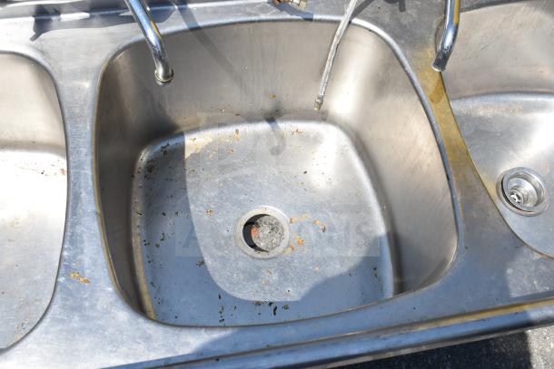 Commercial 3 bay stainless steel sink, no legs, visible signs of wear and some rust spots, fitted with faucets.
