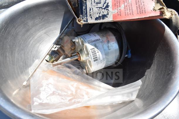 Stainless steel bowl with motor, labels, and packaging inside, part of commercial table contents. Condition: Good.