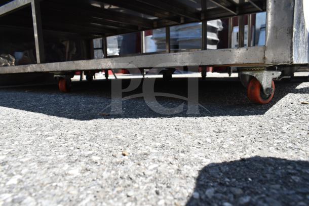 Commercial stainless steel table with under shelves and red caster wheels, suitable for industrial use. Appears in good condition.