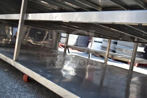 Commercial stainless steel table with under shelves, polished surface, sturdy frame, on caster wheels, ideal for storage.