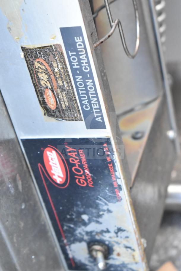 Hatco Glo-Ray food warming strip on metal over shelf. Labels show brand name and caution note. Slight wear visible.