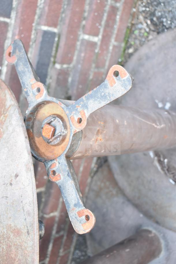Rustic metal table base with four arms, showing signs of wear and weathering.