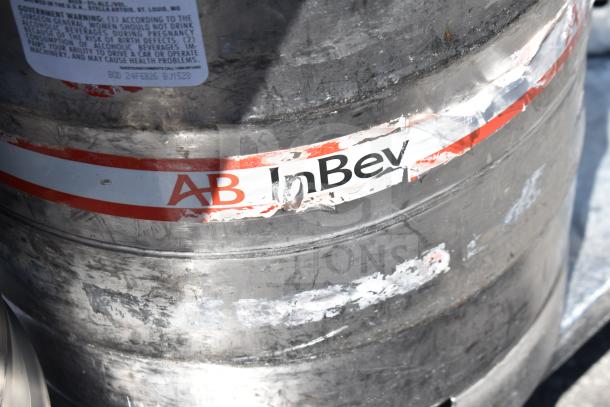 Metal keg with AB InBev label, part of auction lot including a commercial table with under shelf. Keg shows signs of wear.