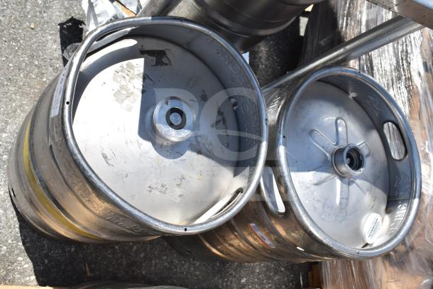 10 half-size metal barrel kegs in used condition, visible brand markings and dents, outdoors on a pallet.
