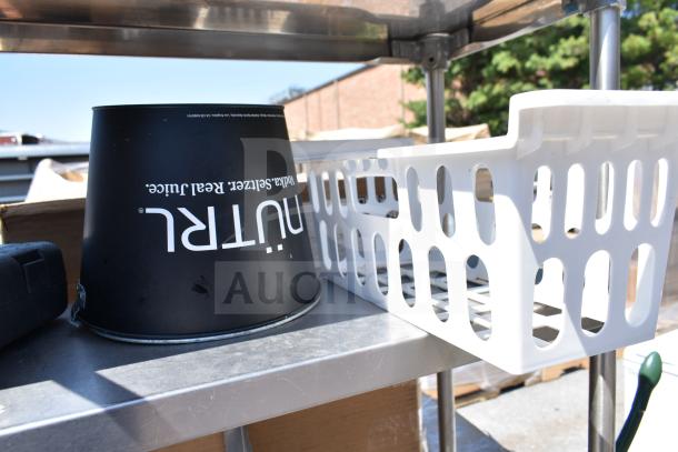 Commercial table with two-tier overshelf and undershelf, includes a black bucket labeled "nutrl" and a white plastic basket.