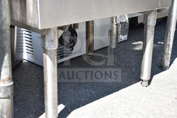 Stainless steel commercial ice bin on sturdy legs, showing signs of wear, with various cables visible. Suitable for restaurant use.