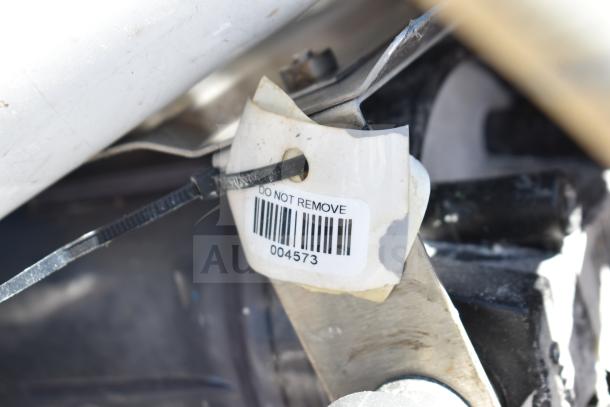 Close-up of a tag labeled "DO NOT REMOVE" with barcode number 004573, attached to metal and cable-tied, part of a mixed lot.