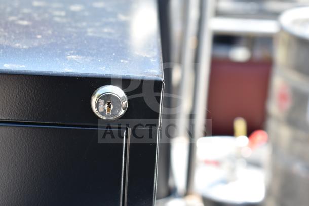 Close-up of Hirsh black four-drawer vertical letter file cabinet lock, showing minor surface scratches.