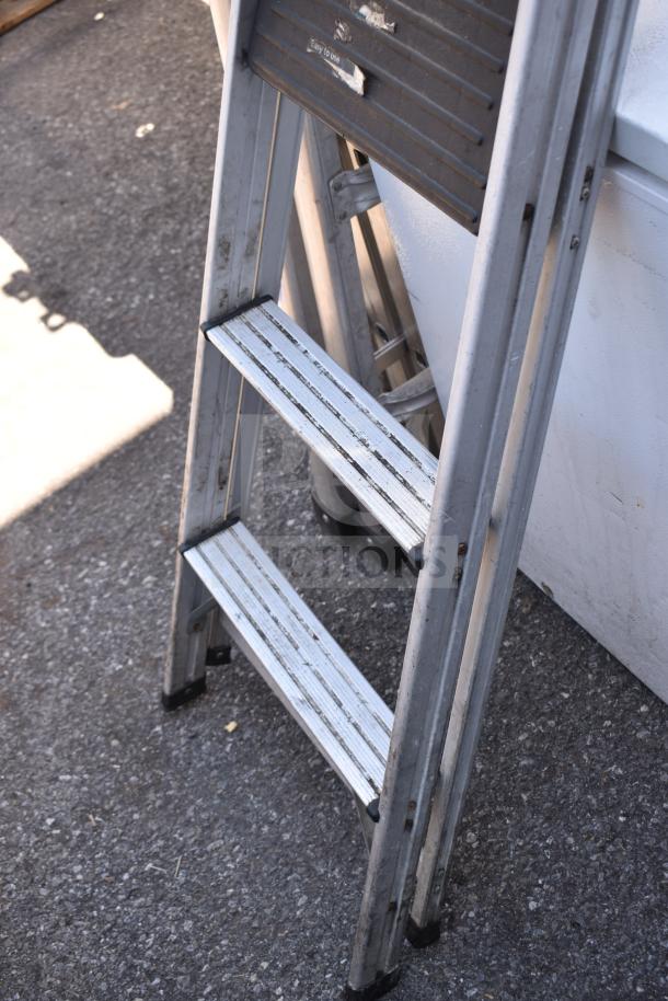 Two aluminum ladders in used condition, showing visible wear. "Easy to Use" label on top section. Auction item: 2 Ladders.