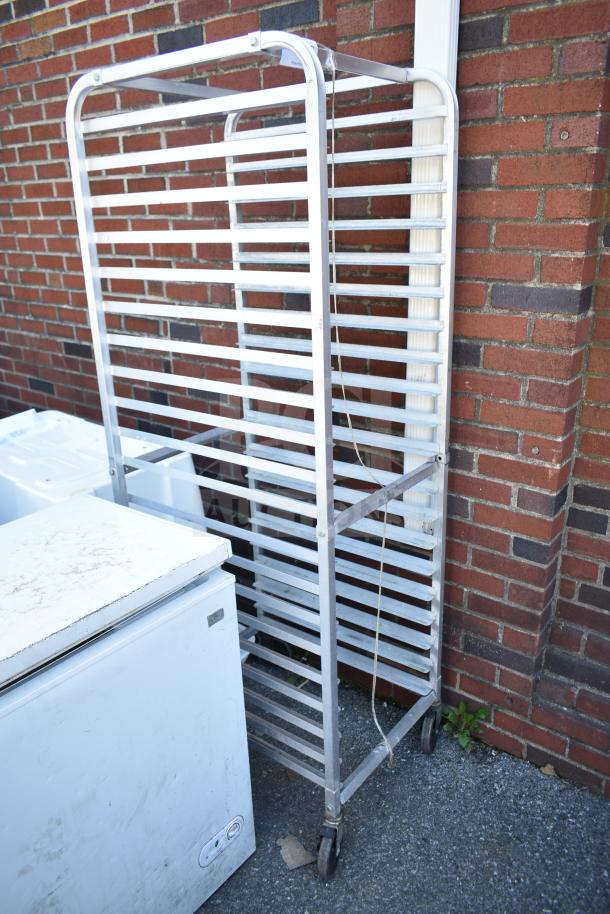 Commercial pan transport rack with multiple shelves on commercial casters, metal frame, good condition, outside brick wall background.
