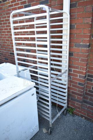 Commercial pan transport rack with multiple shelves on commercial casters, metal frame, good condition, outside brick wall background.