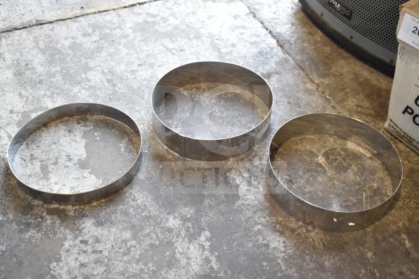Three metal round collars on concrete floor, part of a 12-item auction lot. Reflective surface, good condition.