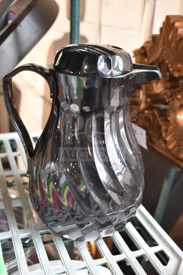 Black pitcher with a reflective, textured design and a handle on a shelf, showcasing a modern aesthetic.
