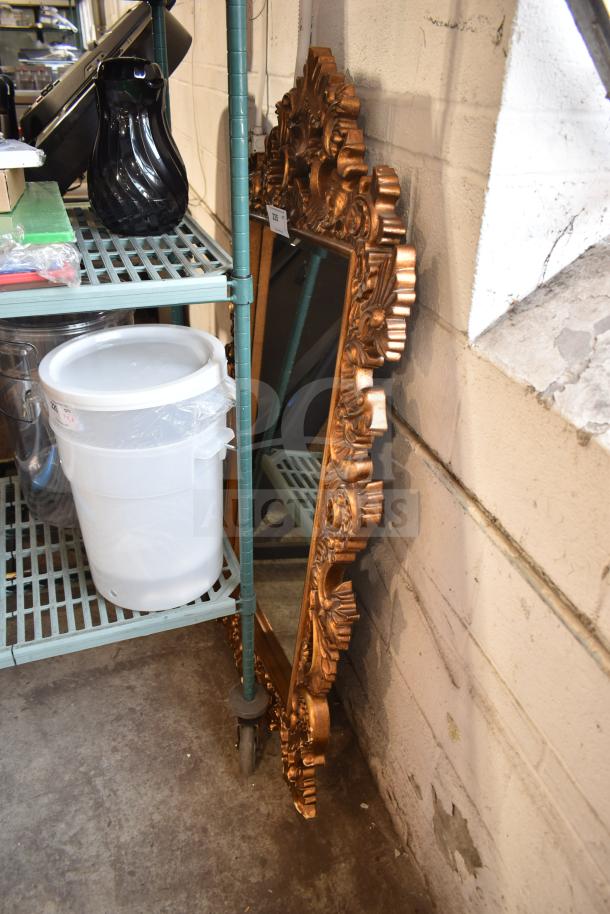 Ornate gold-framed mirror with intricate detailing, leaning against a wall in good condition. Measures approximately 4x2 feet.