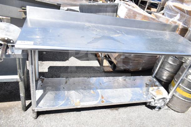 Commercial metal table with under shelf, used condition, visible wear and surface marks, sturdy frame.