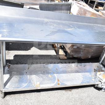 Commercial metal table with under shelf, used condition, visible wear and surface marks, sturdy frame.