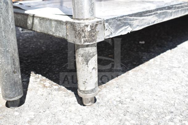 Commercial table corner with metal legs and weathered under shelf. Sturdy design, showing signs of outdoor use.