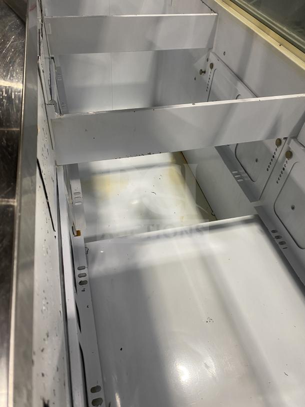 Commercial stainless steel ice cream dipping cabinet with curved glass, rear lift-open access, visible wear inside.