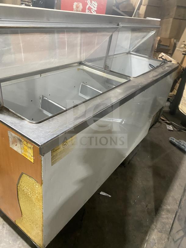Commercial stainless steel ice cream dipping cabinet with slanted glass, rear lift-open access, visible labels, used condition.