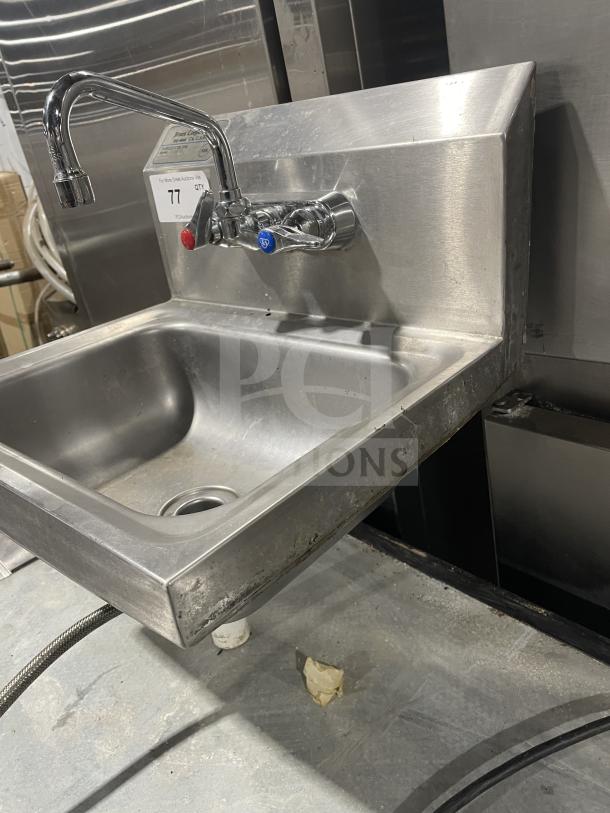 Commercial stainless steel wall-mount hand sink by Jimex with back splash, dual faucet controls, and visible wear marks.