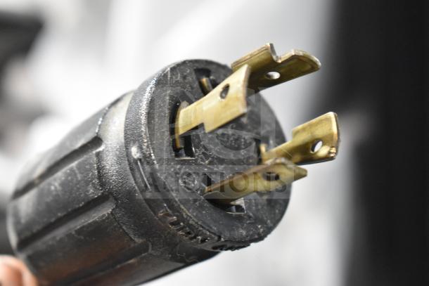 Close-up view of a black electrical plug for the True GDM-49F-HC Freezer, featuring brass prongs, indicating power compatibility.