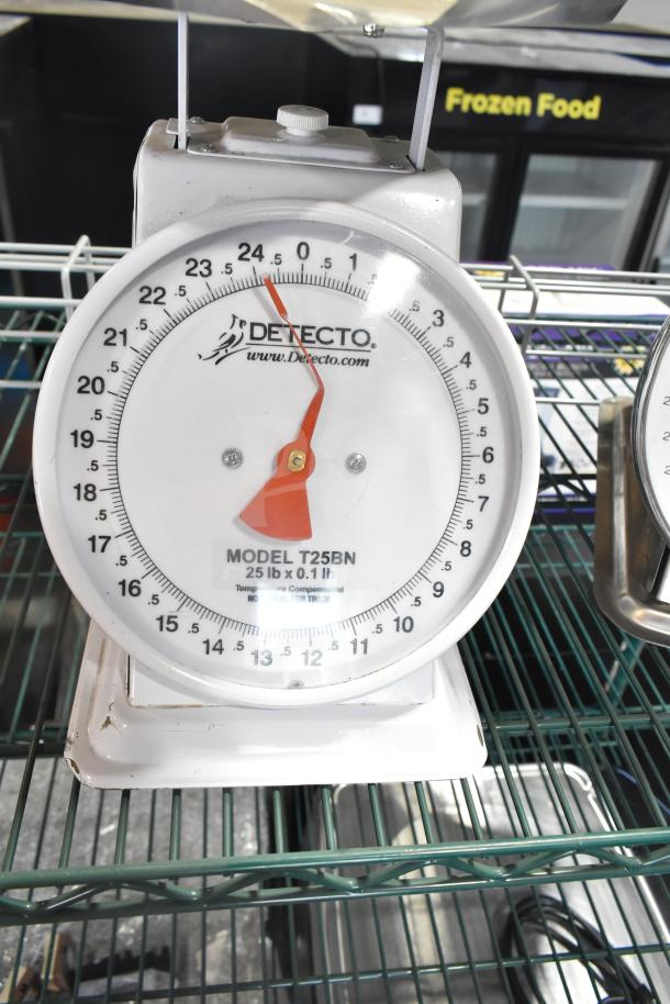 Detecto T25BN scale, 25 lb capacity, white finish with red dial, on green wire rack; visible model and brand marking.