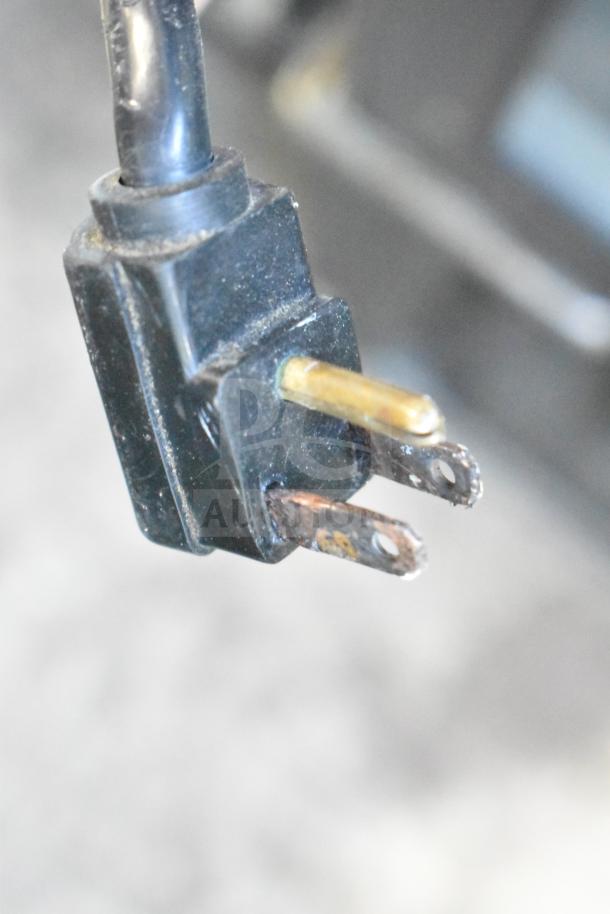 Close-up view of a power cord plug for a Master-Bilt IM-23GB freezer, showing wear on the metal prongs.