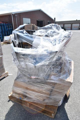 Plastic-wrapped pallet of scratch and dent items, including a work table and glasses, on an outdoor lot. Multiple boxes visible.