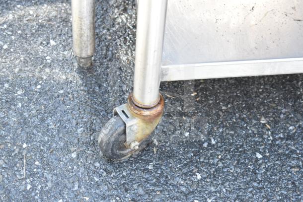 Commercial prep table wheel detail showing metal caster on asphalt. Visible rust on caster, indicating wear.