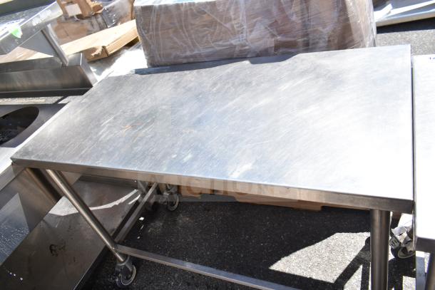 Stainless steel commercial table on casters, sturdy design, some surface scratches, ideal for industrial use.