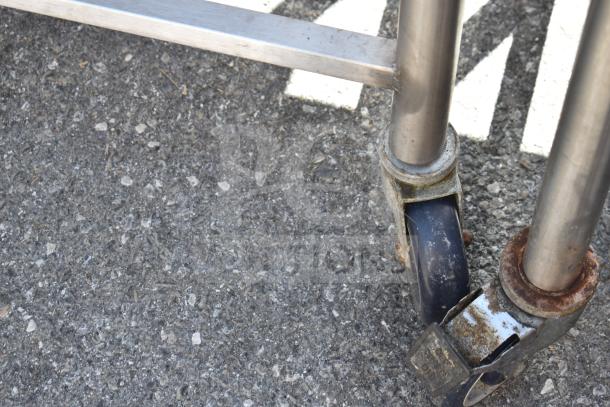 Commercial table on metal casters, showing sturdy, rusted wheels and metallic legs. Ideal for industrial use.