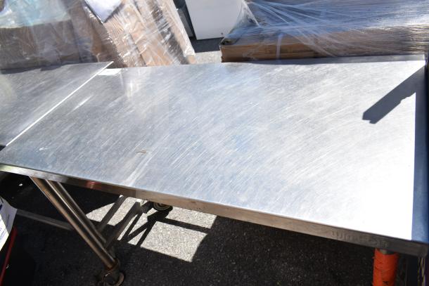 Commercial stainless steel table with commercial casters, showing light surface scratches. Ideal for industrial use.