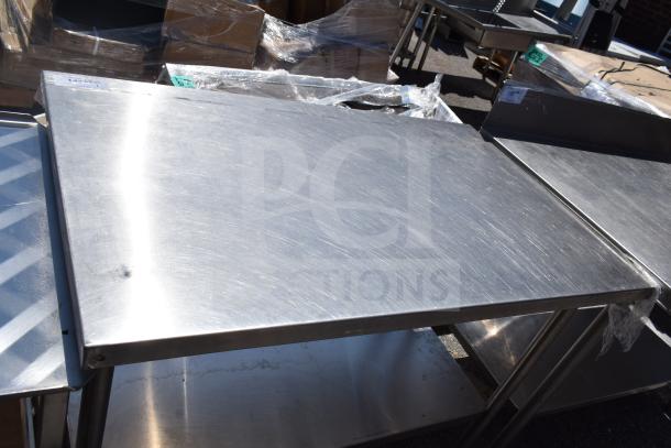 Commercial stainless steel table with under shelf, used condition. Visible scuffs, sturdy design, ideal for food prep or storage.
