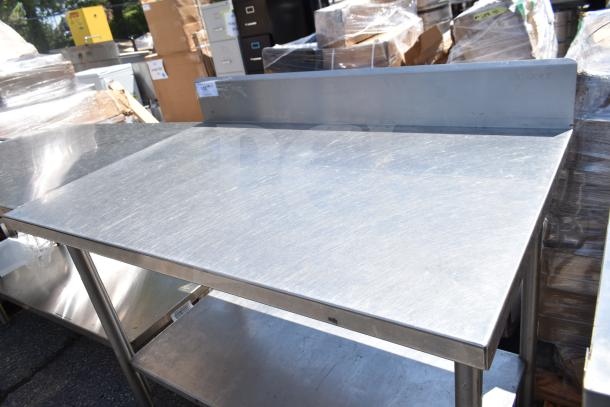 Commercial stainless steel table with backsplash and under shelf, in good condition. Ideal for industrial kitchen use.