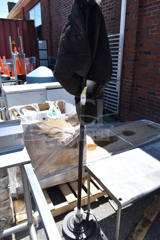 Black vest hanging on a tall lamp with a round base, outdoors. Auction tag visible on lamp pole.