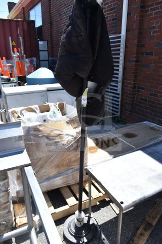 Black vest hanging on a tall lamp with a round base, outdoors. Auction tag visible on lamp pole.