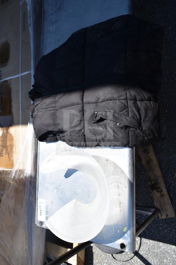 Black quilted vest and translucent lamp shade on a metal table. Vest shows a pocket detail. Lamp shade features a curved design.
