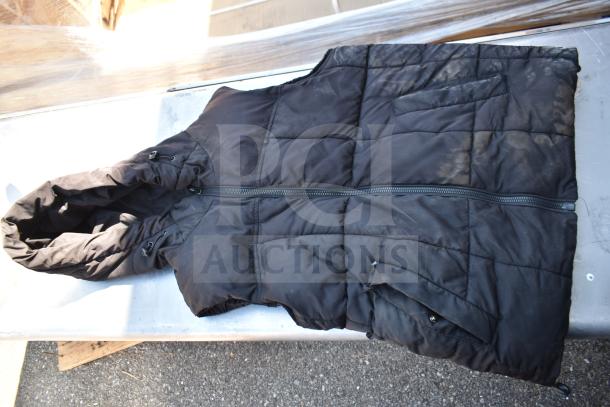 Black puffer vest with hood and zipper, showing signs of wear and dirt on a metal surface.