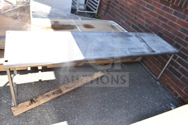 Commercial over shelf, stainless steel, rectangular, slightly worn with visible scuffs, sturdy metal legs, outdoor setting.