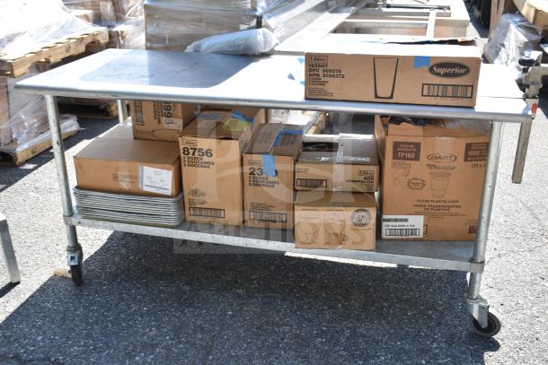 Commercial metal table with boxed contents, including Libbey glassware and baking pans, on wheels. Visible product labels.