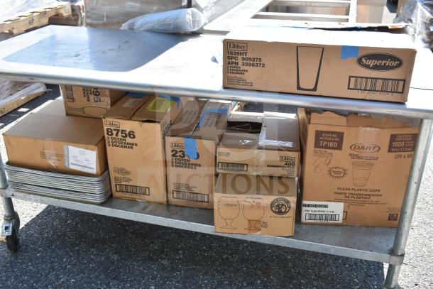 Commercial table with multiple boxes of glasses and baking pans. Labels show brands like Libbey and Dart, indicating contents.