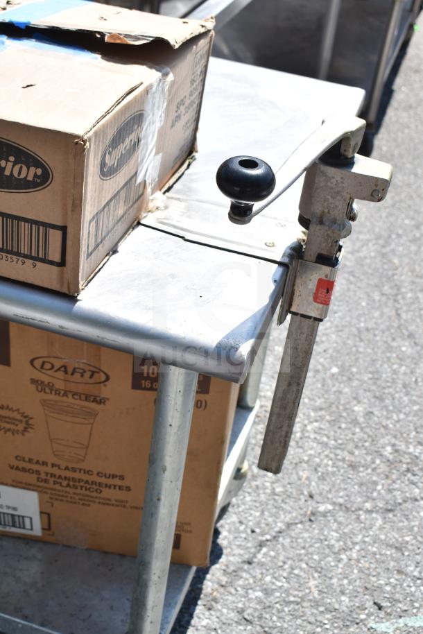 Commercial table with attached manual can opener, includes boxes labeled "Superior" and "Dart" containing glassware and baking pans. Slight wear visible.
