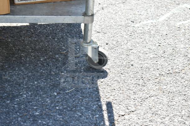 Commercial table on wheels, holding boxes with contents including glasses and baking pans, shown on an outdoor surface.
