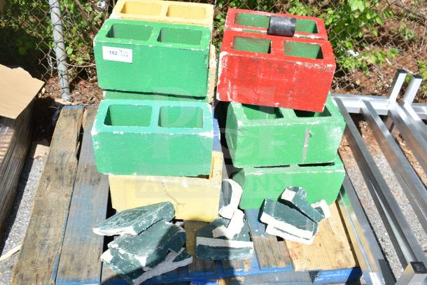 Colorful cinderblocks stacked on pallets; includes green, yellow, and red blocks. Some blocks are broken. Quantity tag visible.