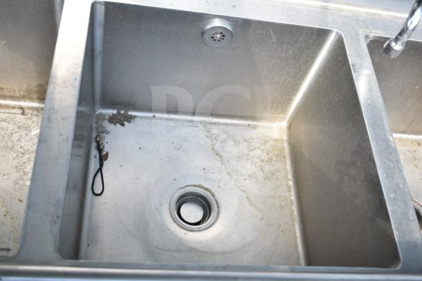 Commercial 3 bay stainless steel sink with dual drain boards, visible wear, suitable for high-volume settings.