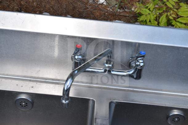 Commercial 3 bay sink with dual drain boards, featuring chrome hot and cold faucets. Stainless steel, moderate wear visible.