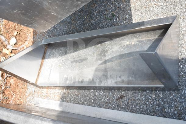 Four metal items including three shelves and a drop-in sink strainer on gravel. Slight wear visible on surfaces.