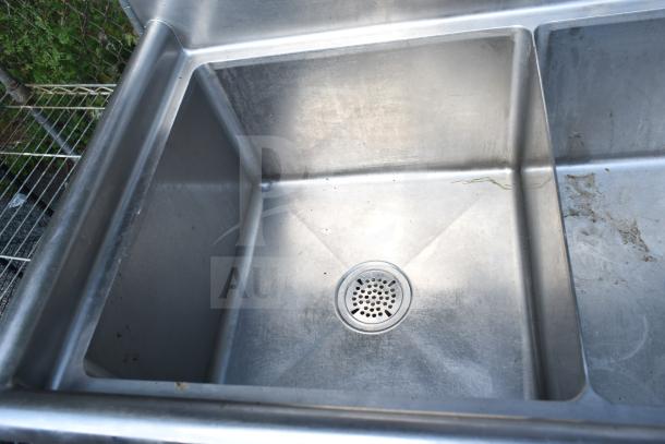 Commercial 2-bay stainless steel sink, slight wear visible, ideal for restaurant use. Features durable construction and drain grates.