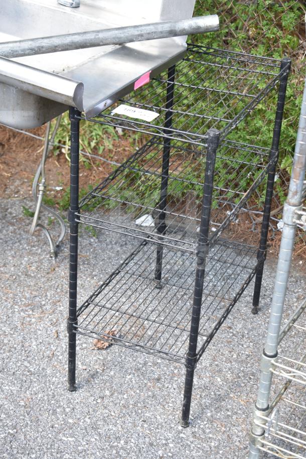 Two black metal wire shelving units with three tiers. Buyer must dismantle. Visible wear, suitable for storage use.